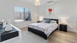 A bedroom with a bed, bedside tables, a desk, a window with blinds, and an air conditioning unit. - Main Street of Goolwa - WIFI, Smart TV, Linen included (Goolwa)