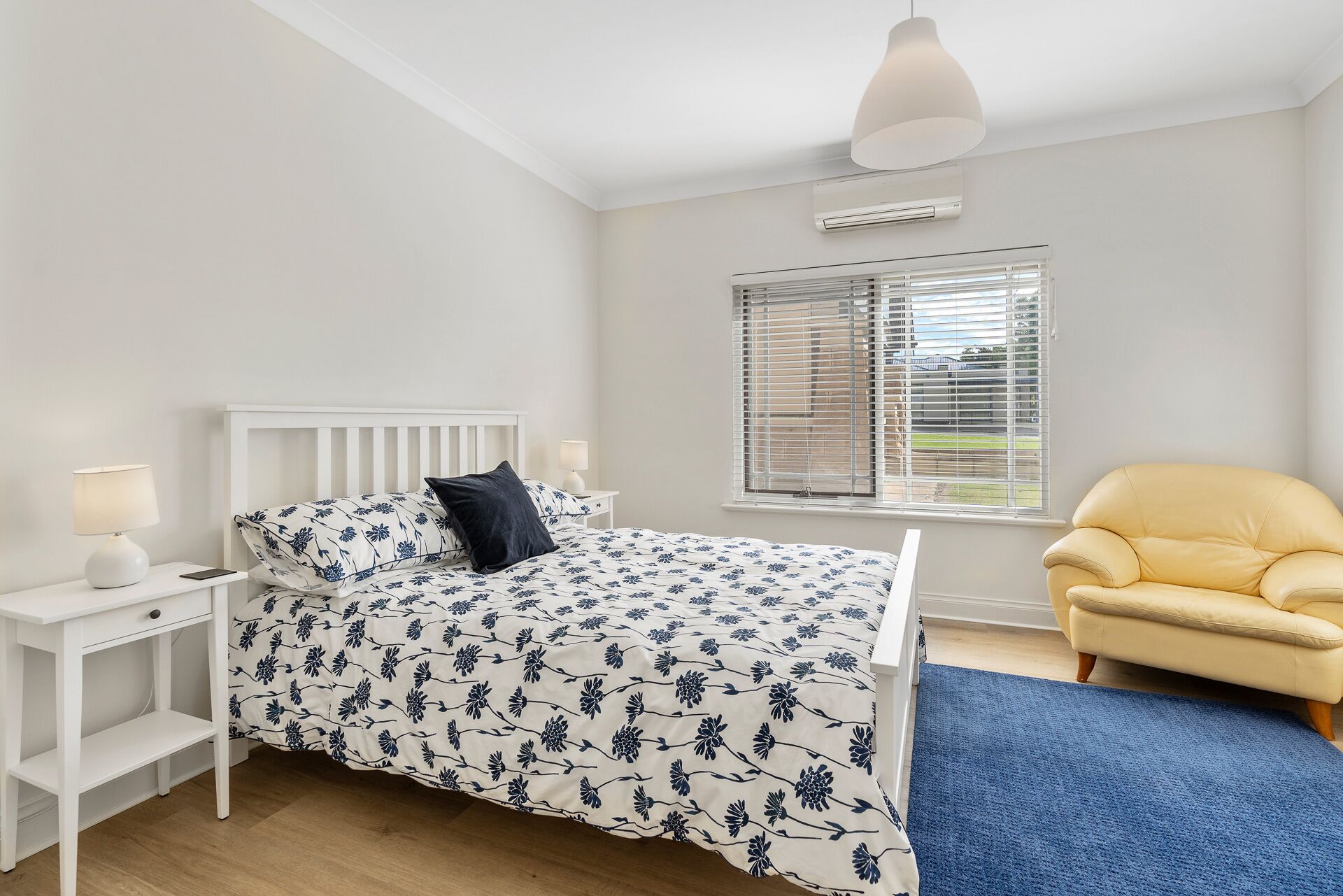 A bedroom with a bed, bedside table, lamp, and a window with blinds.