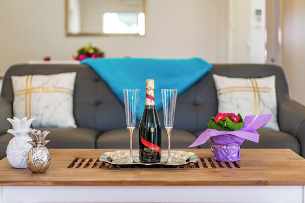 A wooden table with a bottle of champagne, two glasses, a pineapple-shaped salt shaker, and a wrapped gift with flowers. - Main Street of Goolwa - WIFI, Smart TV, Linen included (Goolwa)
