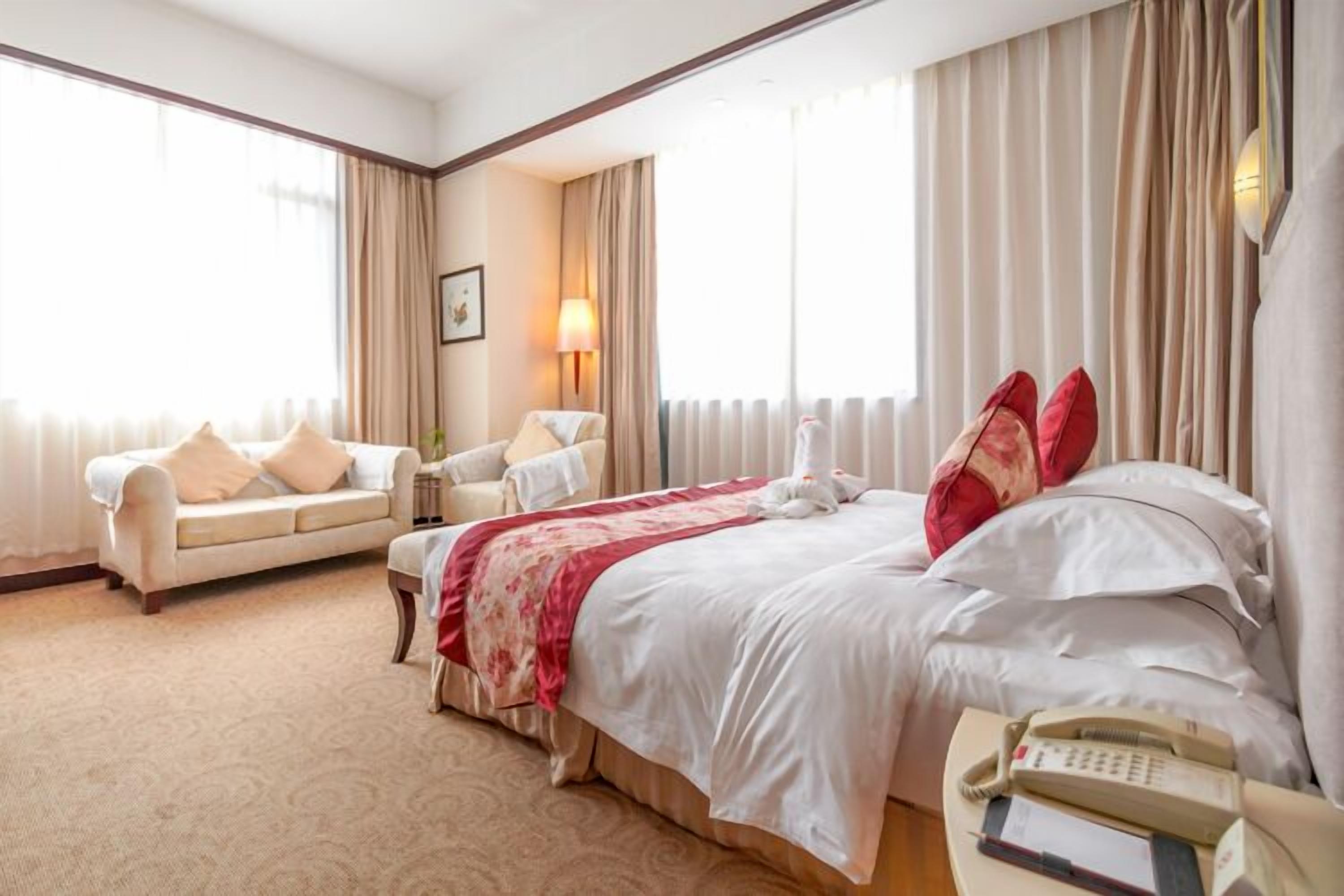 Habitación de hotel con cama, sofá, mesita de noche, lámpara y teléfono.