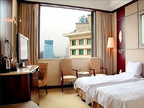 A hotel room with two beds, a desk, a chair, a small table, and a TV.