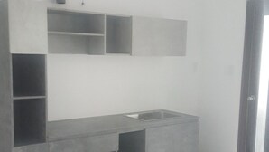 Une pièce moderne et minimaliste, dotée d’un banc intégré et d’une étagère, avec une tuyauterie apparente au plafond et une porte sur le côté droit.