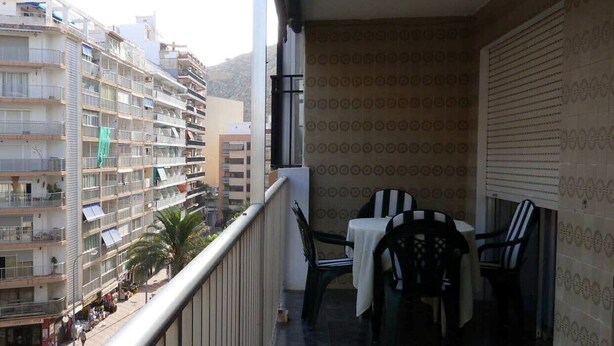 A balcony with a table and chairs, overlooking a cityscape with buildings and palm trees. - Charming 3 bedroom apartment centrally located (Cullera)