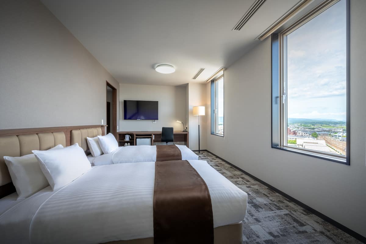 Ett hotellrum med en stor säng, ett skrivbord, en stol, en TV och ett fönster med utsikt över staden.