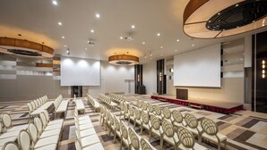 A conference room with rows of chairs, a stage with a red carpet, and large screens. - Hotel Maruya Grande (Minamisoma)