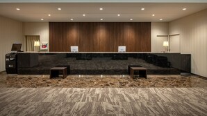 A hotel reception area with a marble counter, two small stools, a reception desk, and a patterned carpet. - Hotel Maruya Grande (Minamisoma)