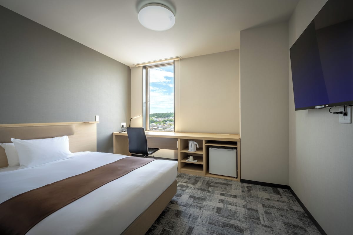 Ett hotellrum med en säng, ett skrivbord, en stol och en tv.