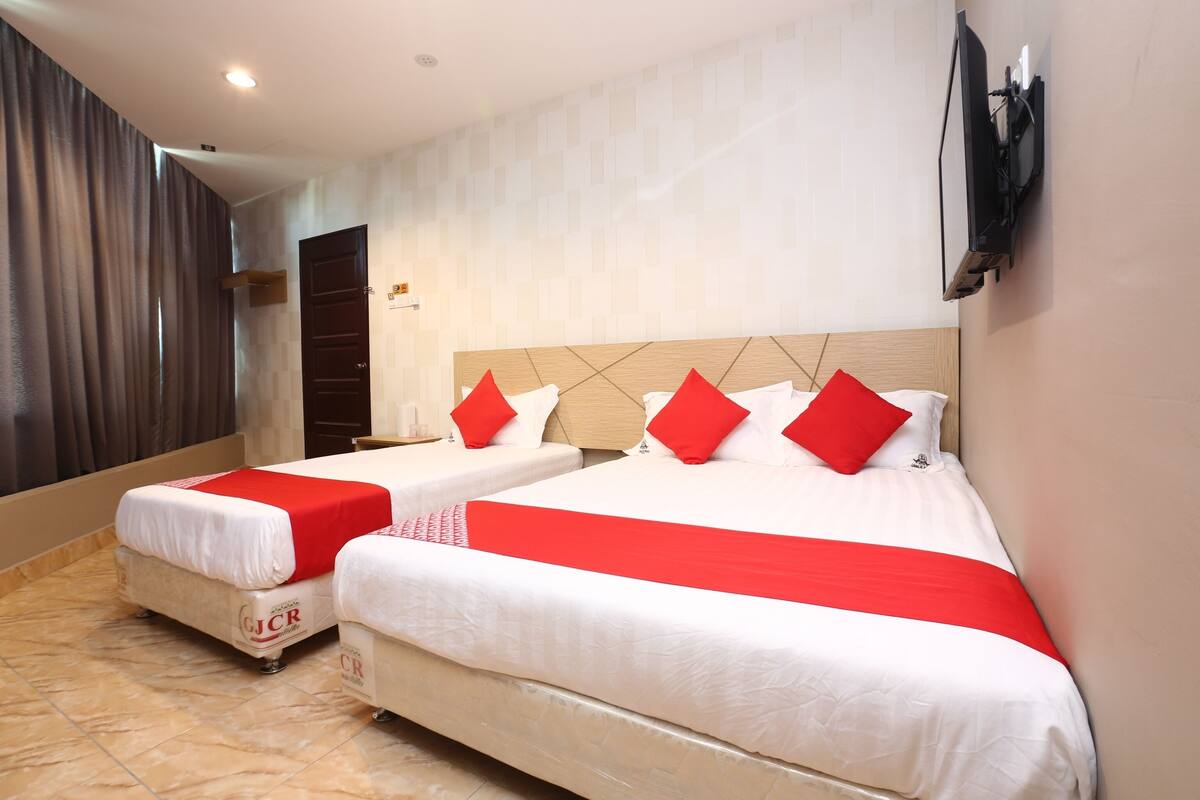 Een hotelkamer met twee bedden, elk met rood-witte beddengoed, een houten hoofdbord en een aan de muur bevestigde televisie.