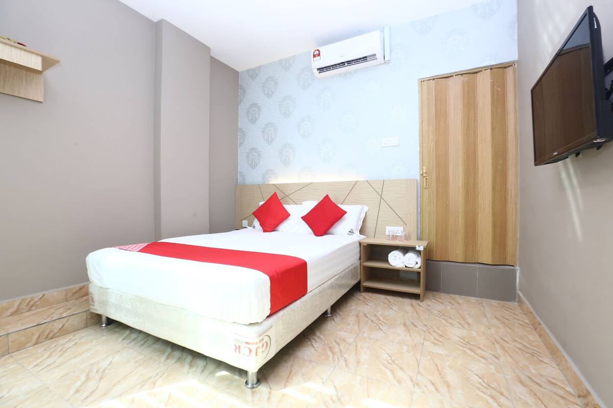 Een hotelkamer met een bed, nachtkastje, kledingkast, televisie en airconditioning.