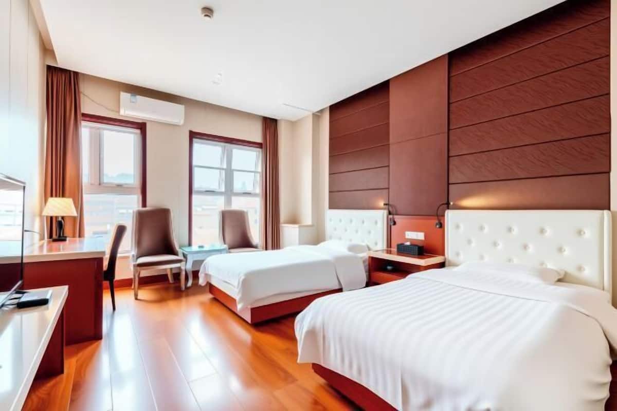 A hotel room with two beds, a desk, a chair, and a window.