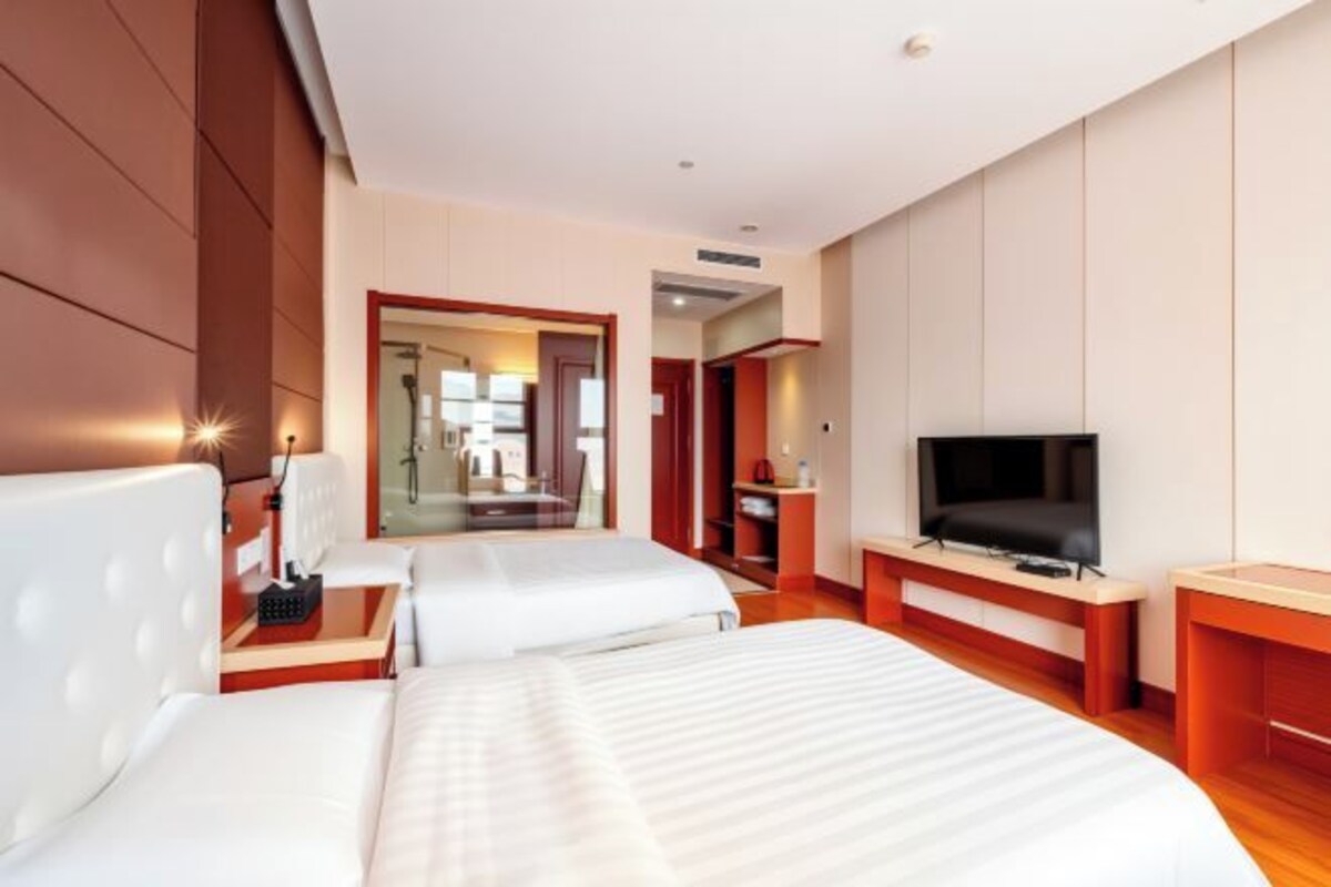 A hotel room with two beds, a TV, a desk, and a bathroom visible through an open door.