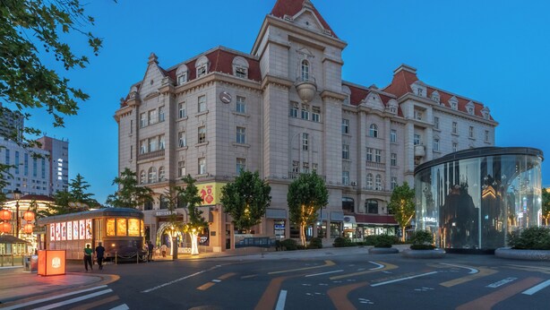 A large, historic building with a prominent tower, a tram stop, and a glass structure. - Huaqi Kaiserdom Hotel (Qingdao)