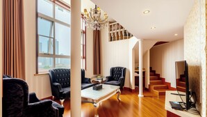 A modern living room with a large window, a chandelier, a staircase, and a flat-screen TV. - Huaqi Kaiserdom Hotel (Qingdao)
