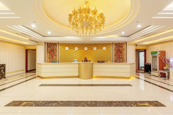 A hotel reception area with a grand chandelier, a reception desk, and a wall clock.