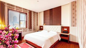 A hotel room with a large bed, a desk, a chair, a nightstand, a lamp, and a vase with flowers.