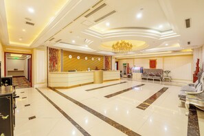 A hotel lobby with a reception desk, seating area, and a chandelier.