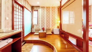 A traditional Japanese-style room with tatami flooring, a low wooden table, a sofa, a television, and a small refrigerator. - Huaqi Kaiserdom Hotel (Qingdao)