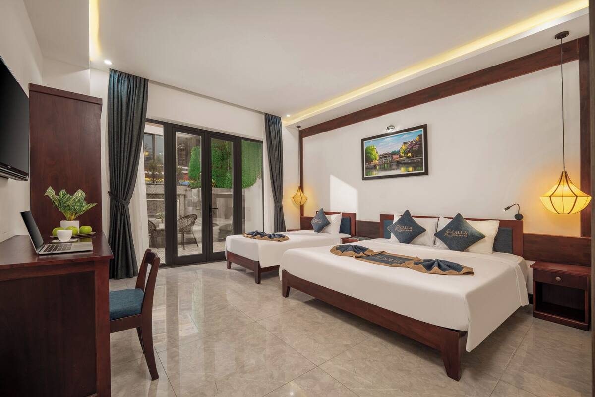 A hotel room with two beds, a desk with a laptop, a chair, a TV, and a view of the outdoors.