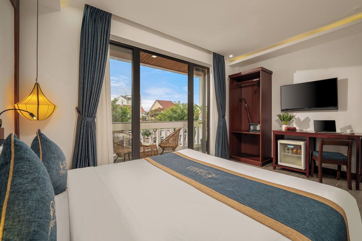 A hotel room with a large bed, a TV, a desk, and a view of the outside.