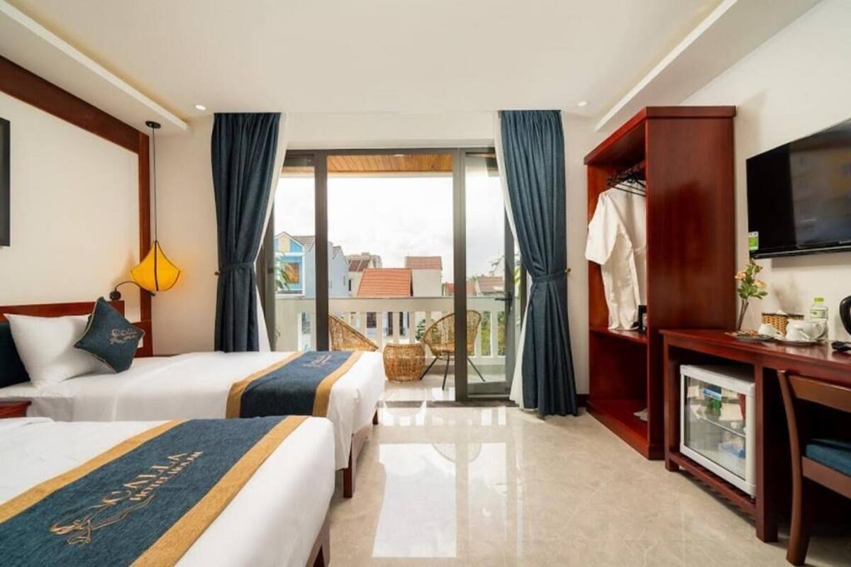 A hotel room with two beds, a TV, a balcony with a view, and a wooden desk.