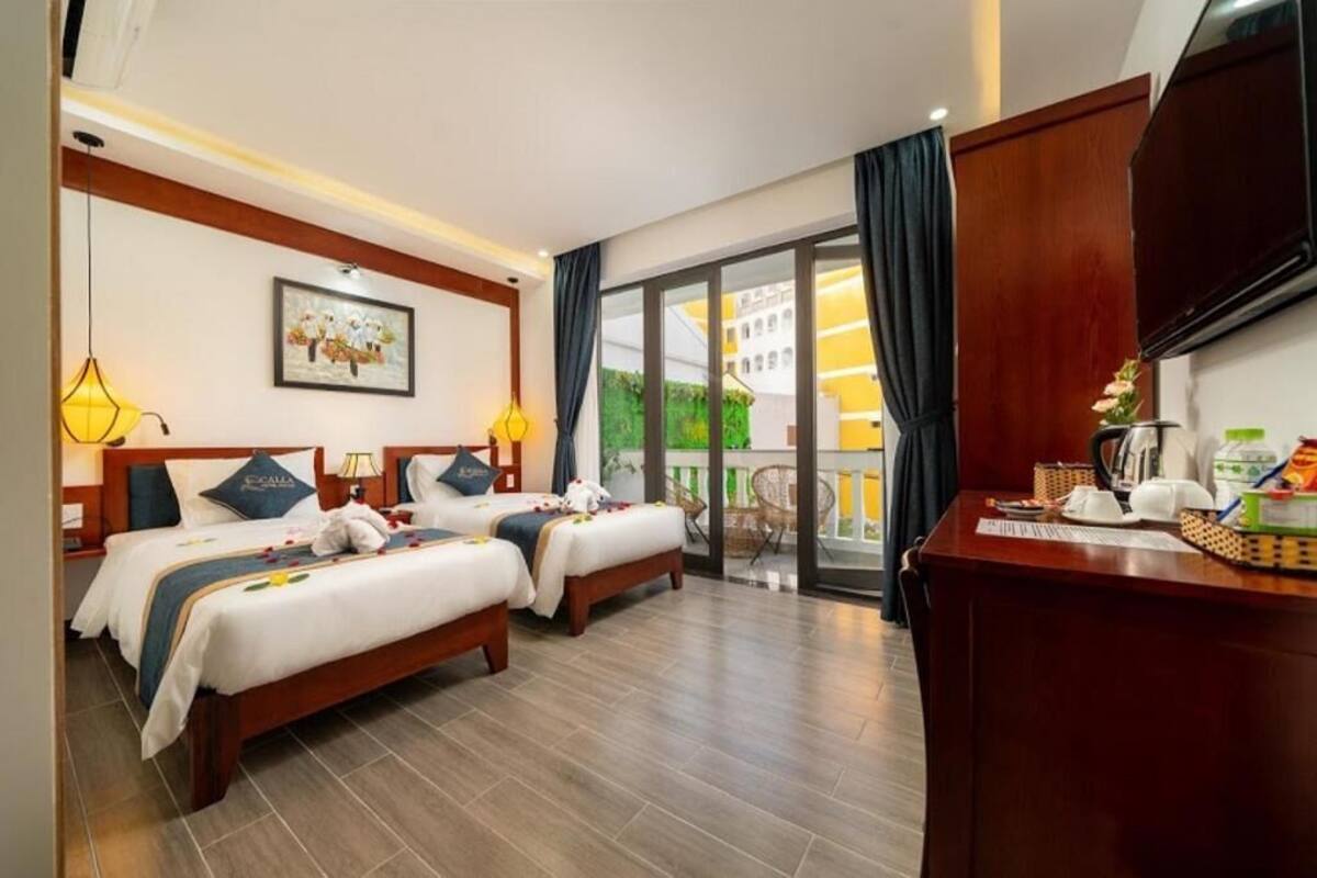 A hotel room with two beds, a desk with a flat-screen TV, a balcony with a view, and a painting on the wall.