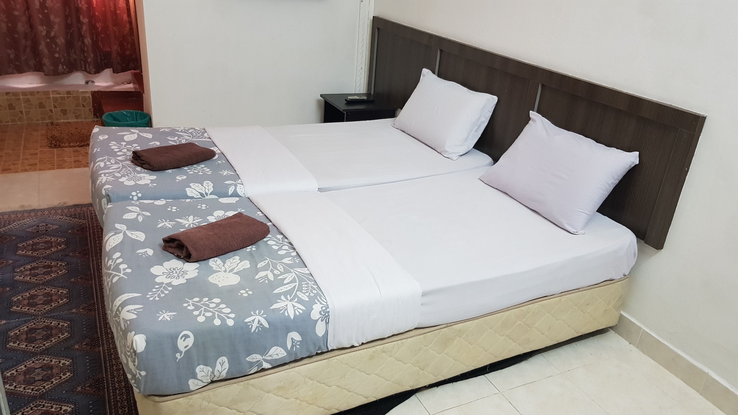 A double bed with a quilted headboard, two pillows, and two folded towels.