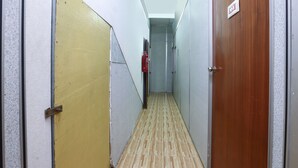 A narrow hallway with a yellow door on the left, a wooden door on the right, and a fire extinguisher mounted on the wall. - OYO 89755 D&d Budget Inn (Kota Bharu)