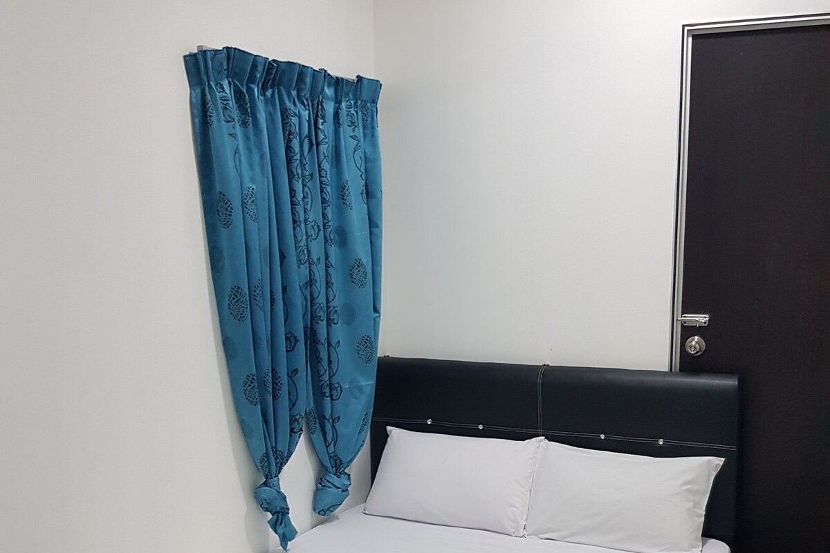 A single bed with a white mattress and pillows, a black headboard, and a blue curtain with a floral pattern.