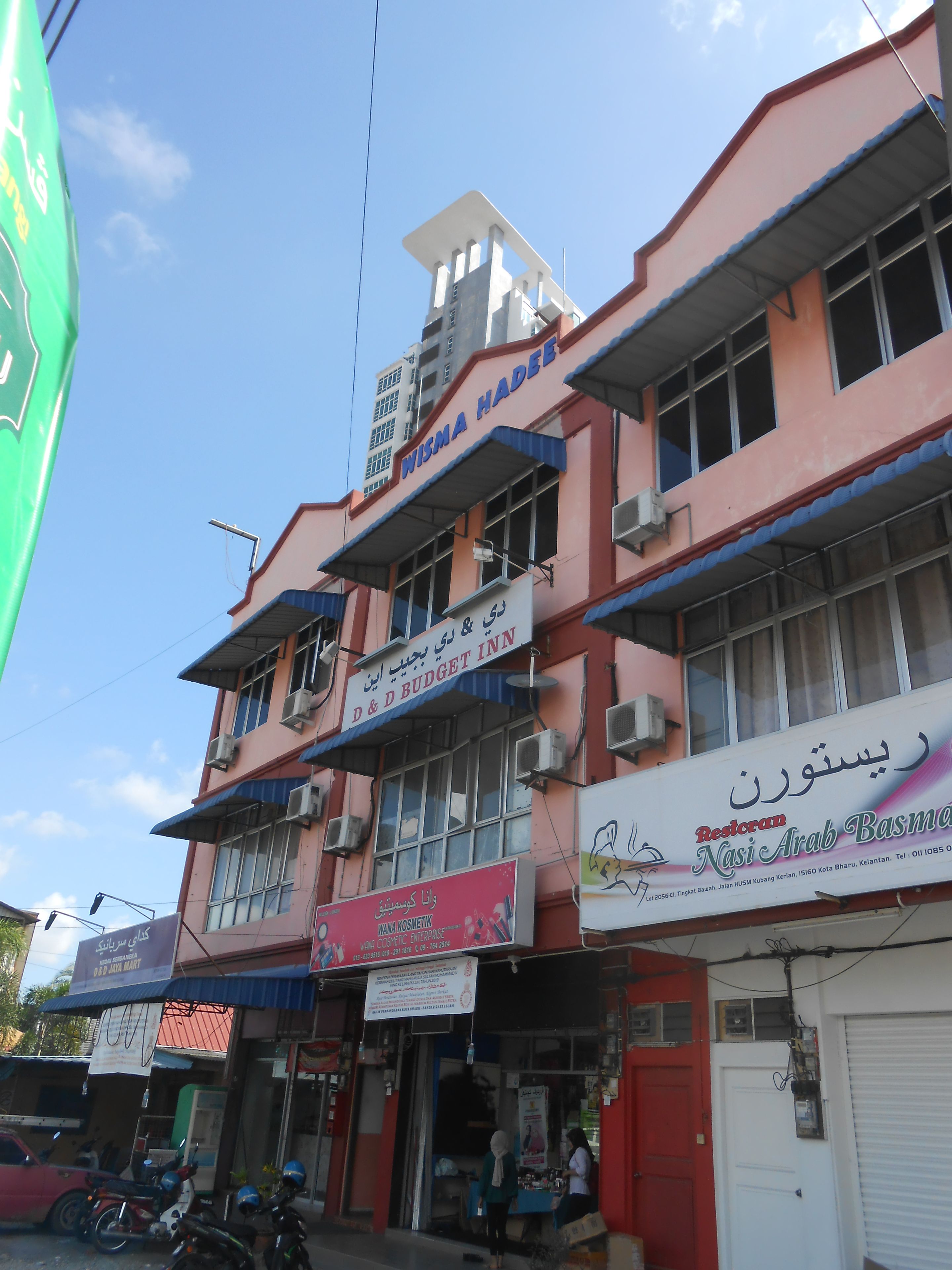 A multi-story building with various commercial establishments on the ground floor, including a budget inn and a cosmetic shop.