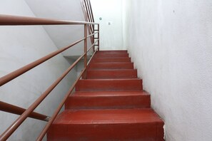 A staircase with red steps and a metal handrail, leading to a white wall with a green exit sign. - OYO 89755 D&d Budget Inn (Kota Bharu)