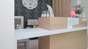 Mostrador de recepción con una barra blanca, un adorno de pared, una lámpara y un cartel con los horarios de registro de entrada y salida.