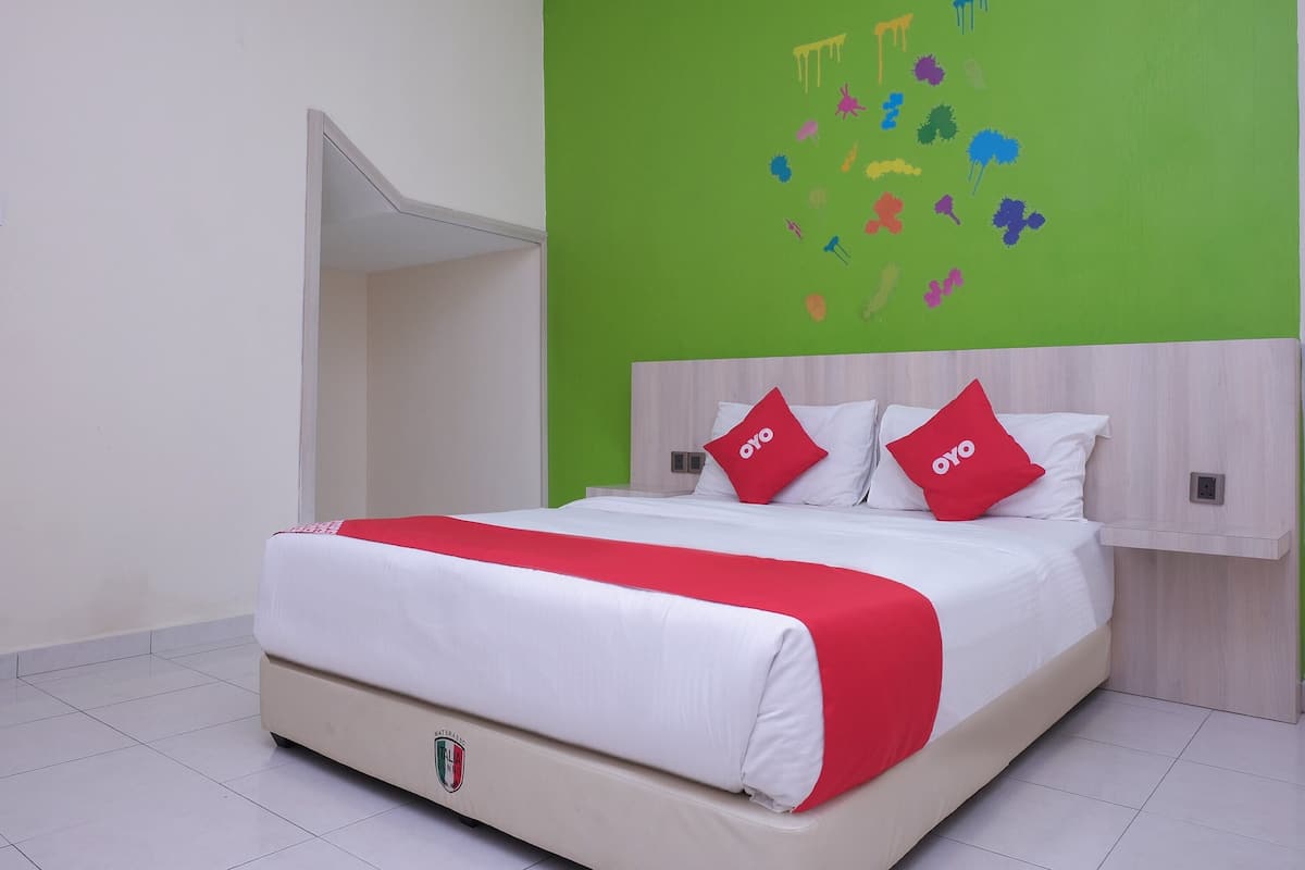 Una cama bien hecha con ropa de cama blanca y roja, una pared verde con arte mural colorido y un cabecero de madera.