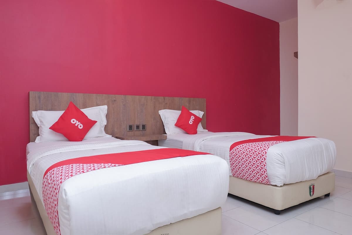 Una habitación de hotel con dos camas, cada una con cabecero de madera, ropa de cama blanca y almohadas rojas.