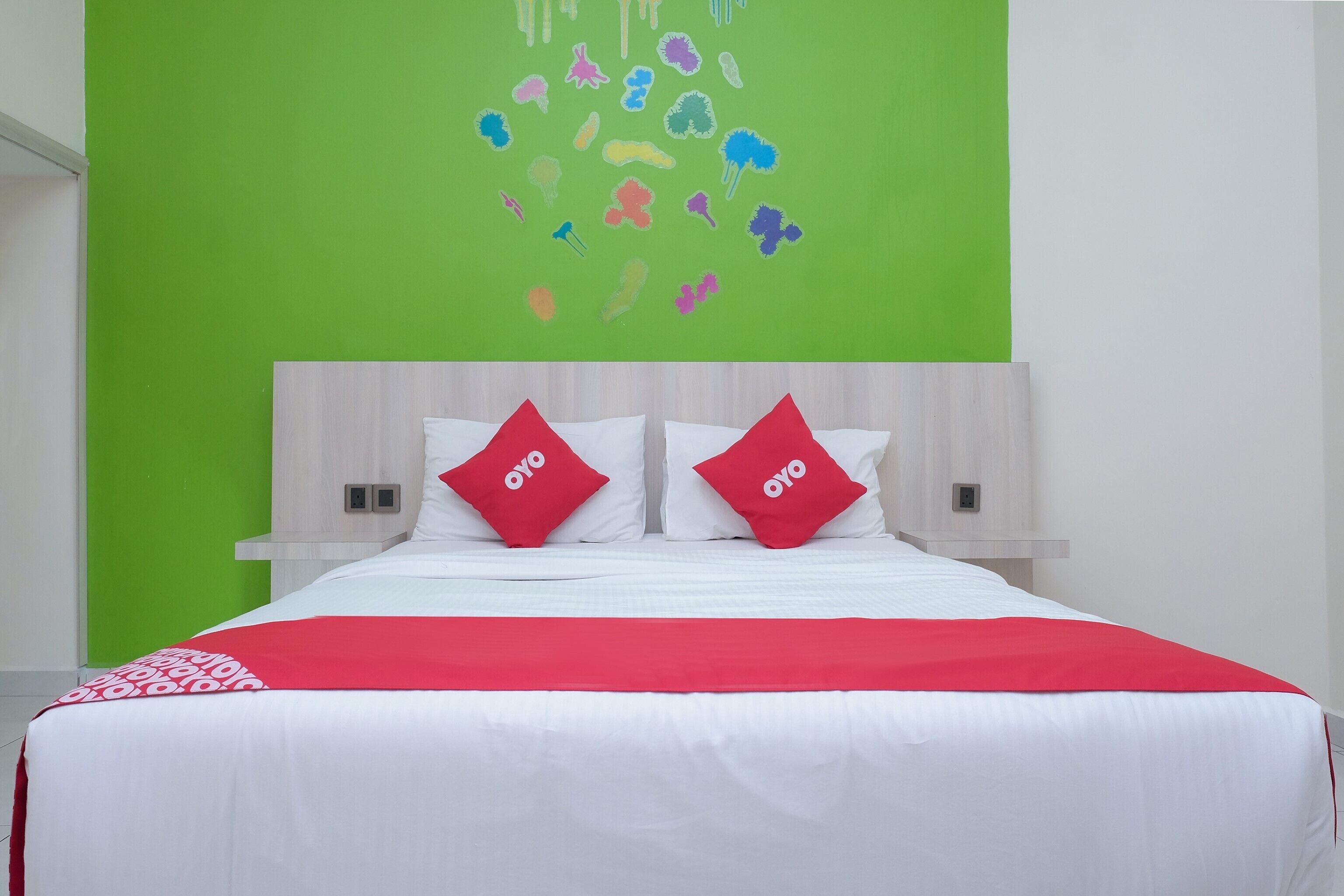A hotel room with a bed, two red pillows, a green wall, and a white headboard.