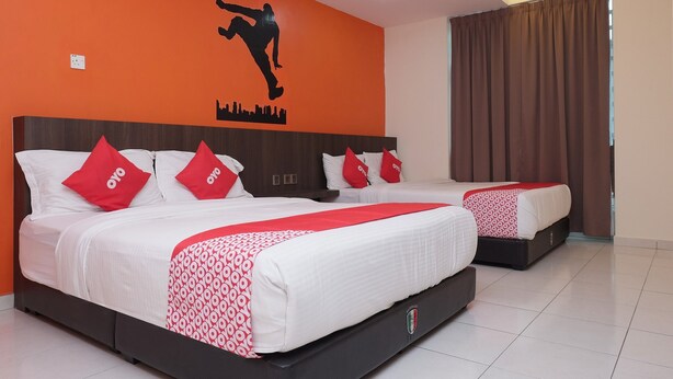 Habitación de hotel con dos camas, cada una con ropa de cama blanca y almohadas rojas, un mural de un horizonte urbano en la pared y cortinas marrones.