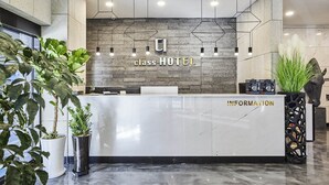 A hotel reception desk with a stone wall backdrop, a reception counter, and potted plants.