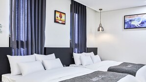 A hotel room with two beds, dark curtains, a painting on the wall, and a hanging light fixture.