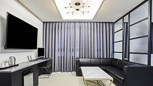 A modern living room with a flat-screen TV, a sofa, a coffee table, and a large window with blinds.