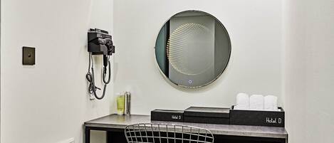 A hotel room with a hairdryer, a mirror, a towel rack, and toiletries on a counter.