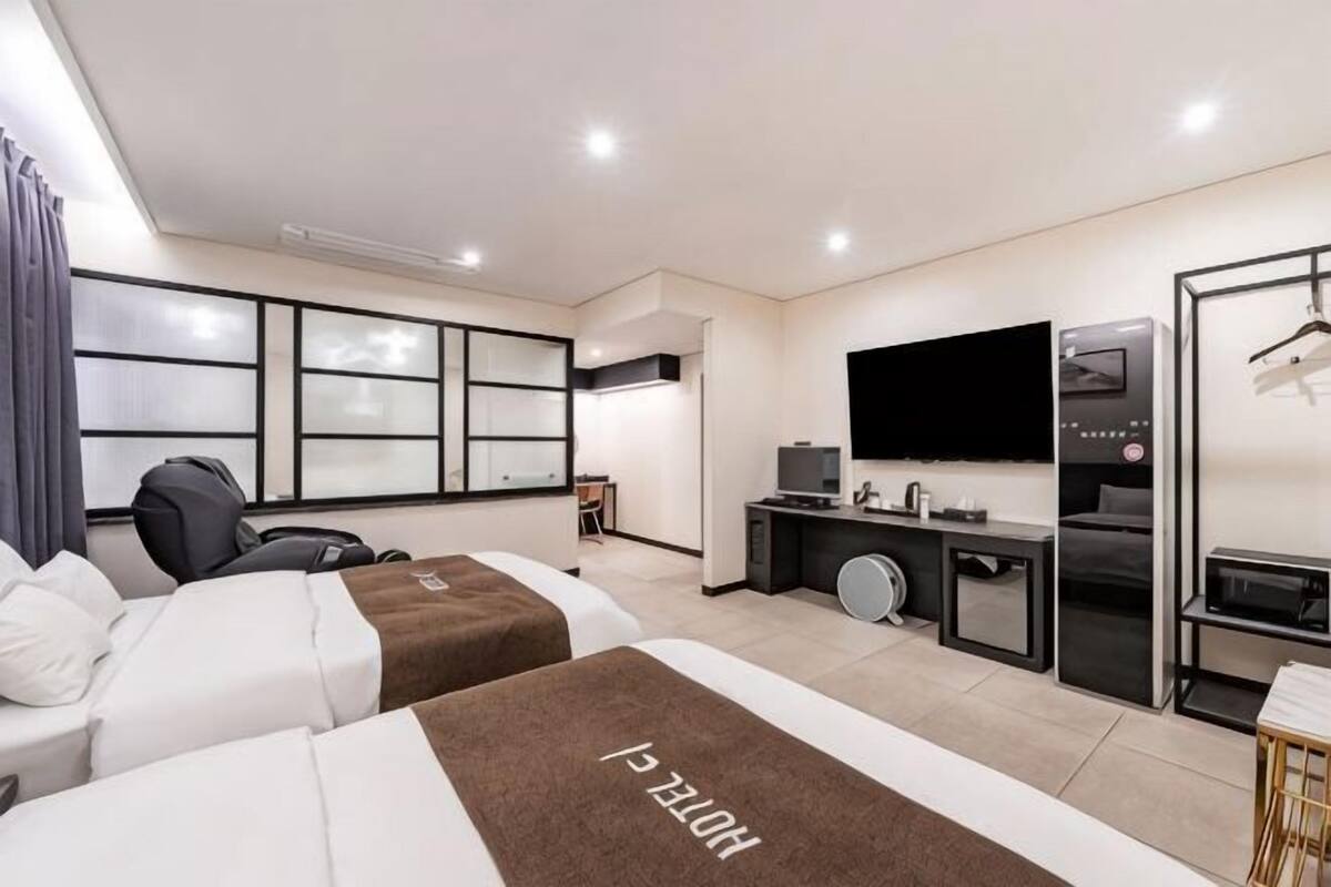 A hotel room with two beds, a desk with a computer, a TV, and a minibar.