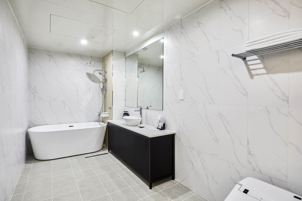 A modern bathroom with a freestanding bathtub, a black vanity, a large mirror, and a towel rack.