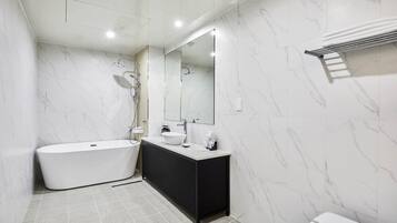 Un baño moderno con una bañera independiente, un mueble de tocador negro, un espejo grande y un perchero para toallas.