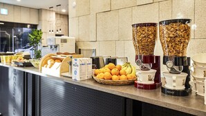 A breakfast buffet with cereal, fruits, and coffee mugs.