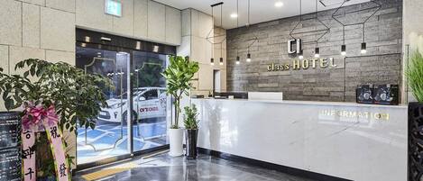 A hotel reception area with a modern design, featuring a marble counter, a reception desk, and a wall-mounted sign that reads "CLASS HOTEL".