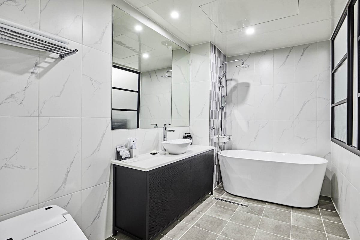 A modern bathroom with a freestanding bathtub, a large mirror, and a vanity with a sink and towel rack.