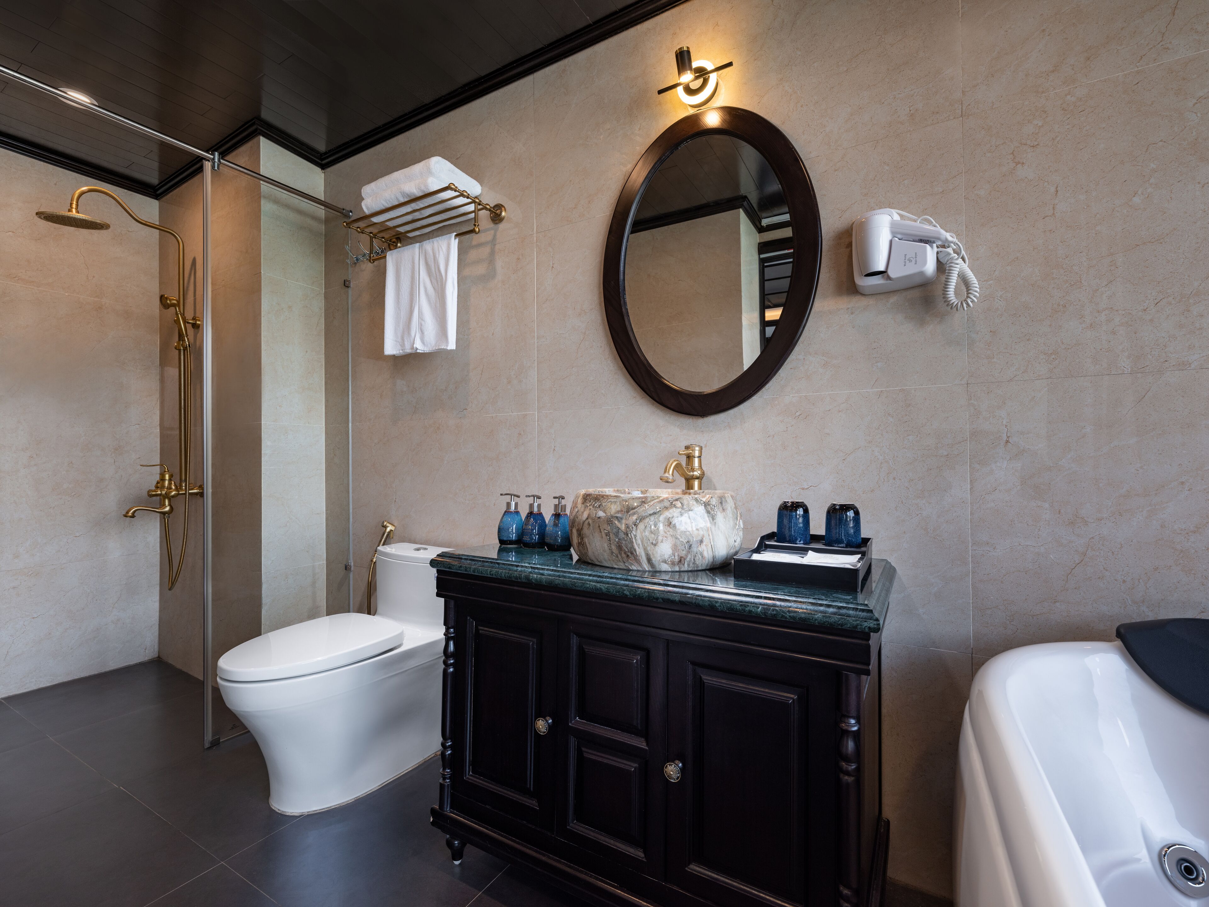 Un baño moderno con ducha de vidrio, inodoro blanco, lavamanos de mármol con grifo dorado y tocador negro.