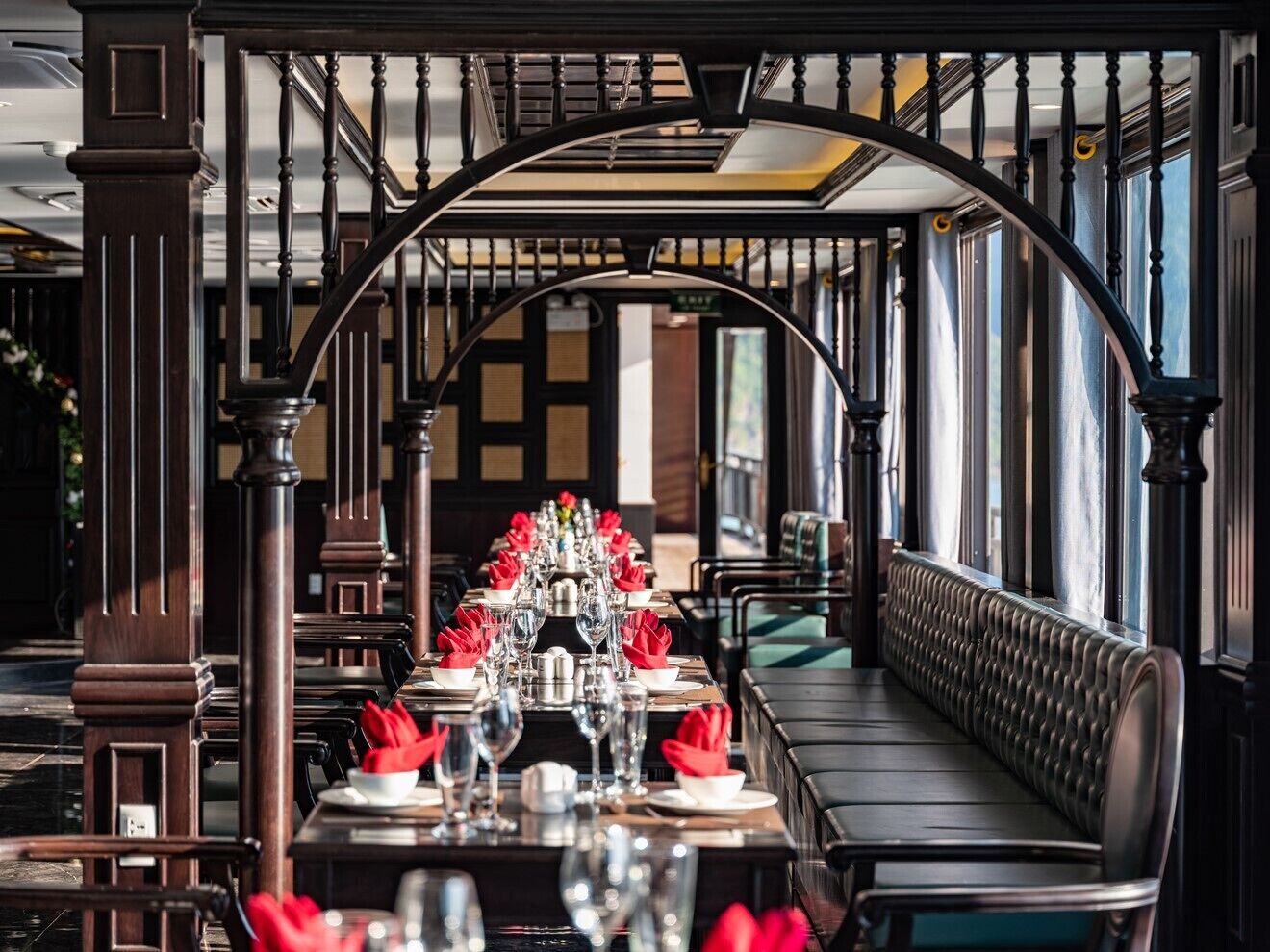 Un restaurante con una larga mesa dispuesta para una comida, una banca a lo largo de la pared y una escalera con barandilla curva.