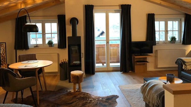 A cozy loft-style room with a fireplace, a dining area, and a seating area with a TV. - Bodenschneid Suites Neureuthblick - Bodenschneid Suite Neureuthblick (Kreuth)