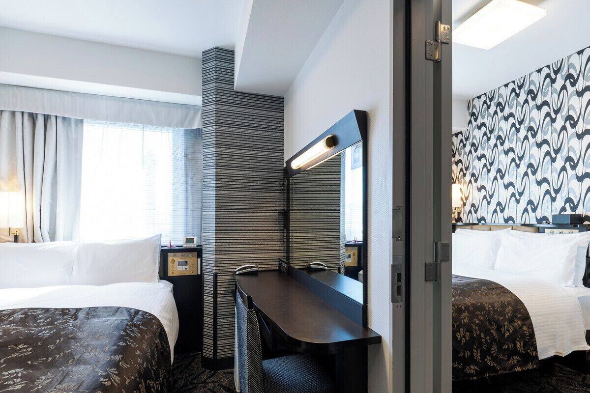 Ein Hotelzimmer mit zwei Betten, einem Schreibtisch mit Spiegel, einem Sessel, einem Nachttisch und einer Wand mit Muster.