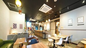 A modern cafe with wooden tables and chairs, a bar area, and a seating section with a green couch. - APA Hotel Nambaminami Ebisucho Eki Shinsekai (Osaka)